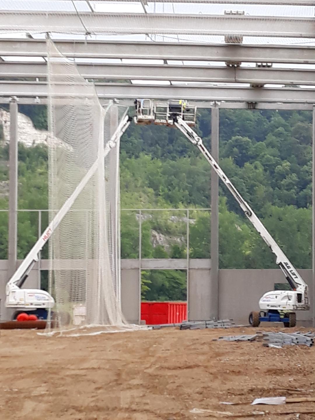 Deux nacelles élévatrices installent un filet sur un bâtiment en construction.