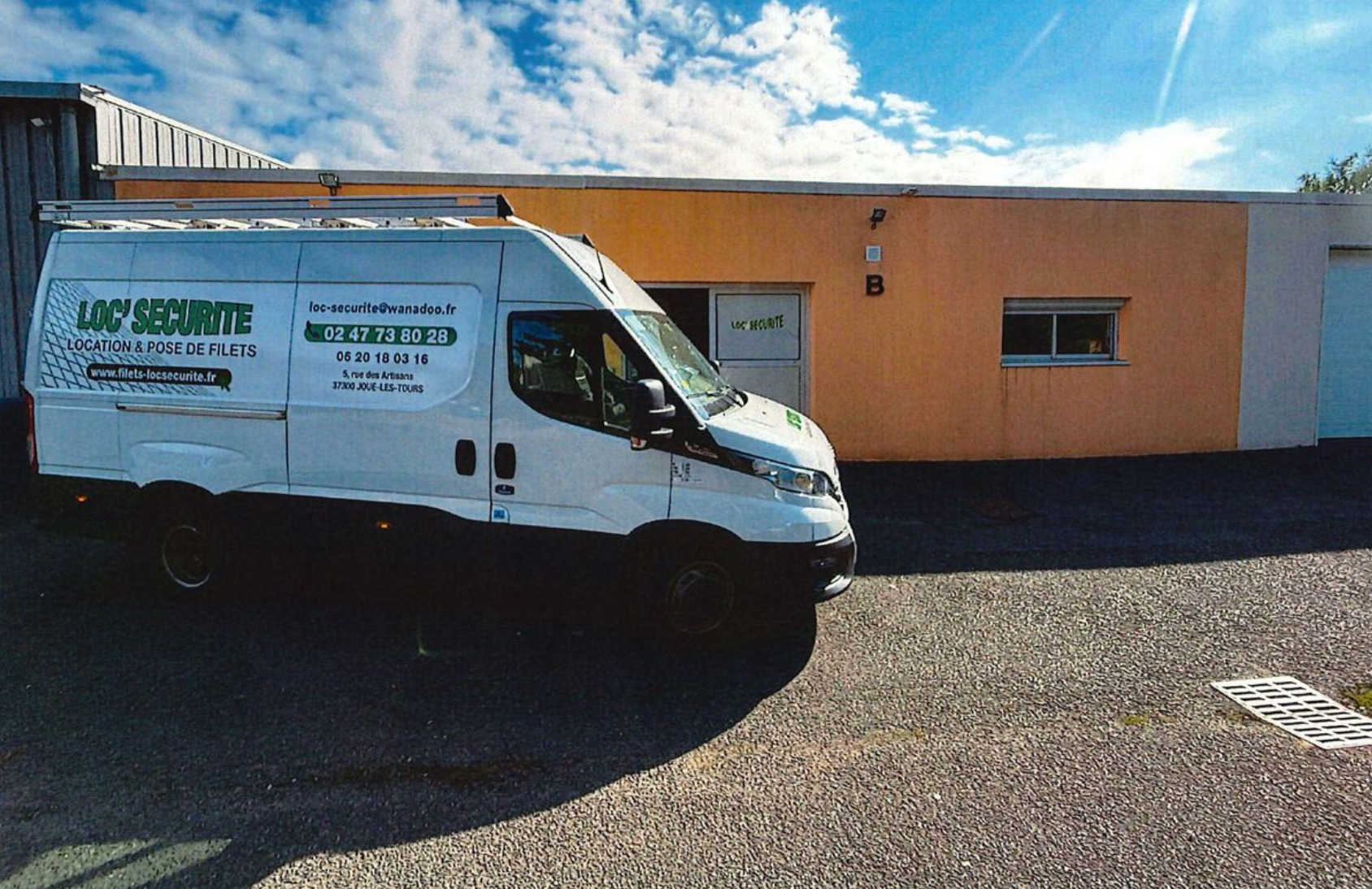 Fourgon de Loc Securité stationné devant un bâtiment orange sous un ciel nuageux.