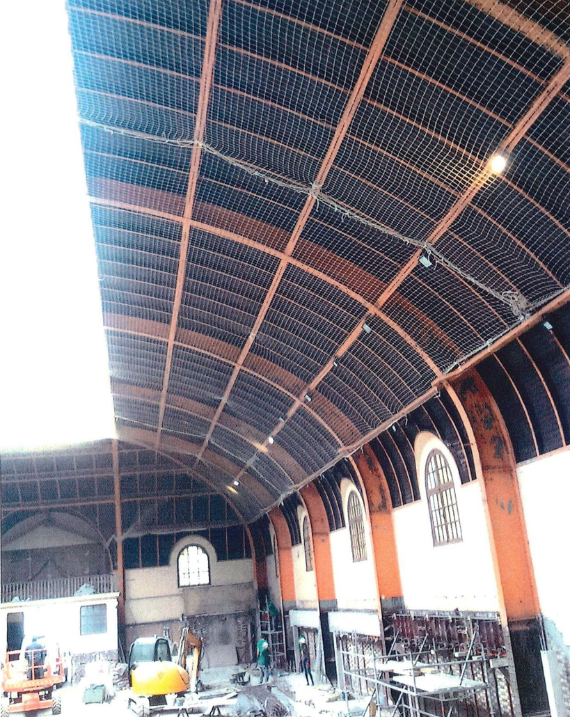 Vue intérieure d'un bâtiment montrant un plafond incurvé avec des filets de sécurité.