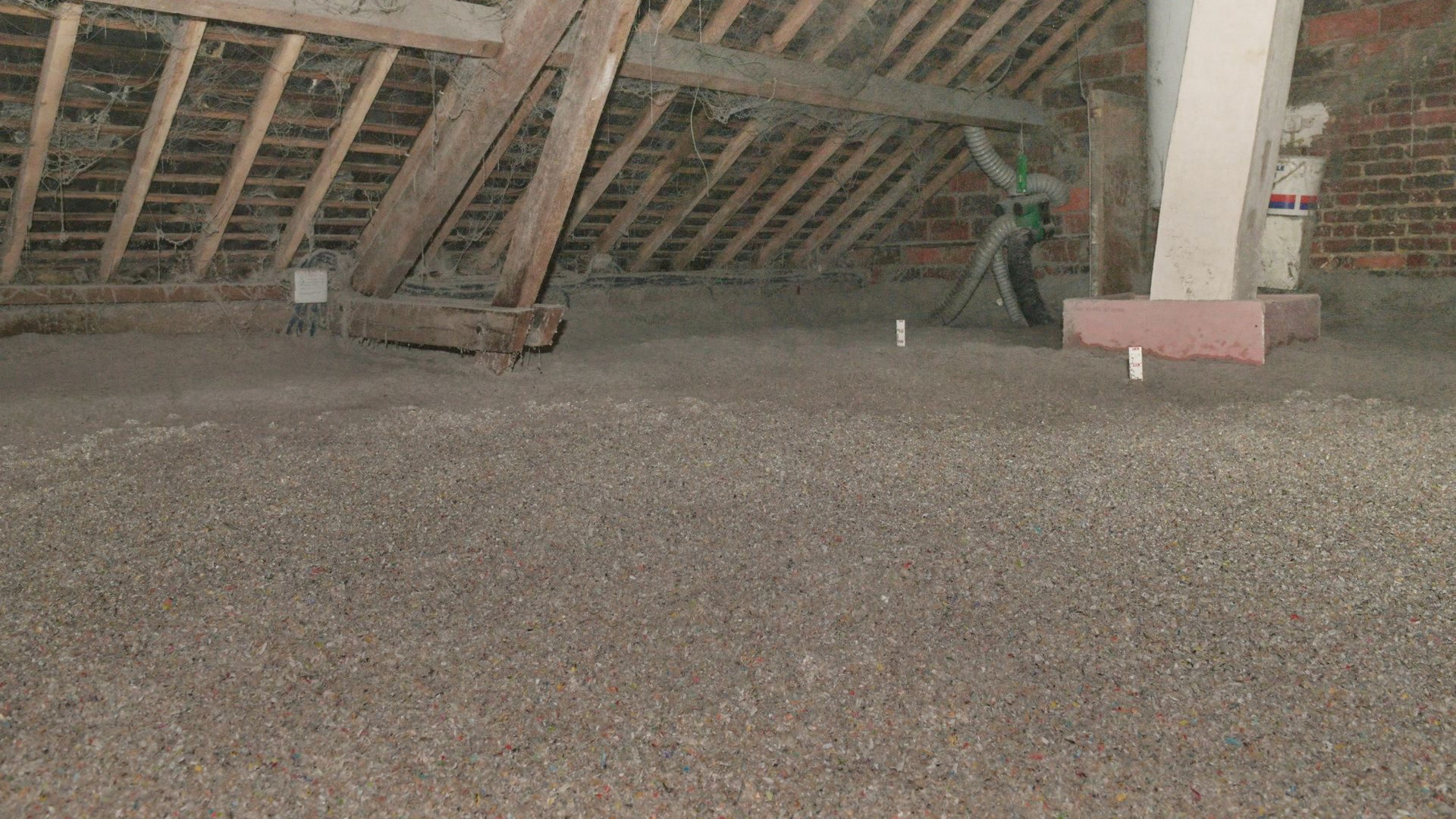 Grenier avec poutres en bois et isolation au sol.