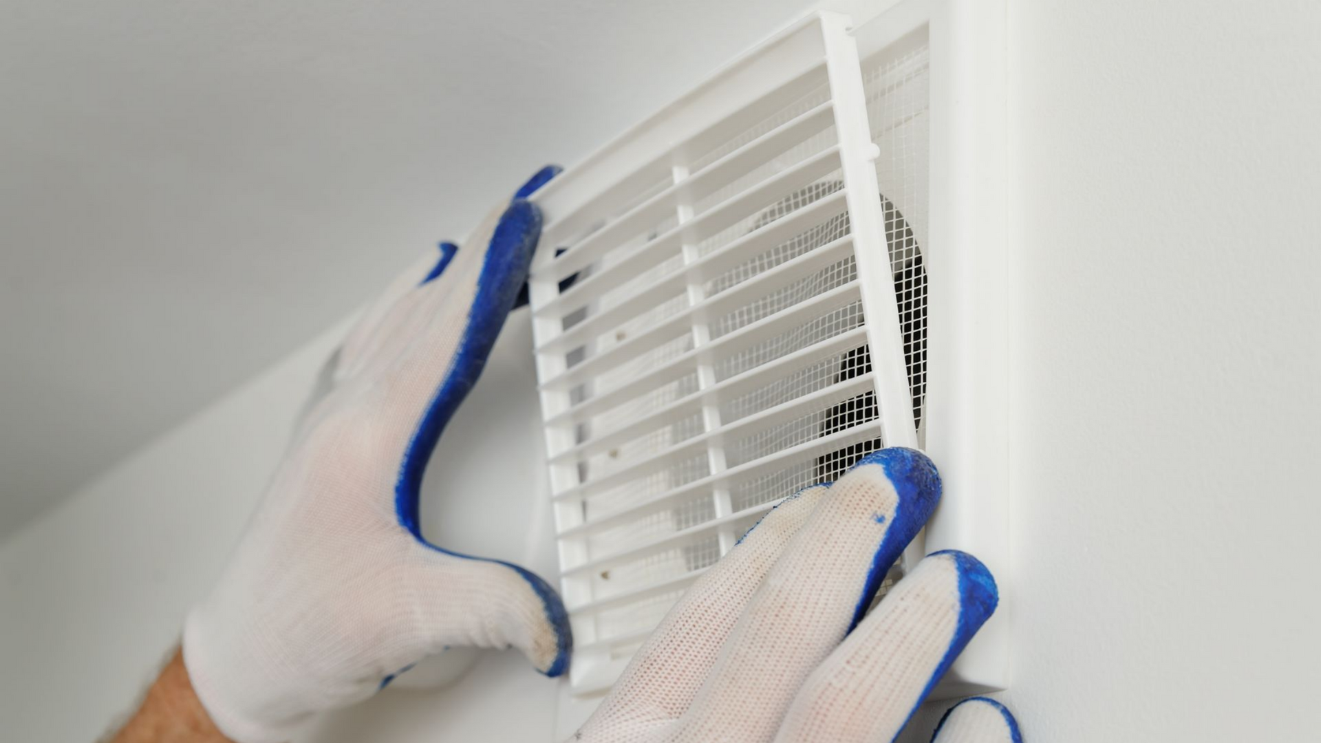Des mains gantées de bleus et de blancs retirent une grille d'aération blanche d'un mur.