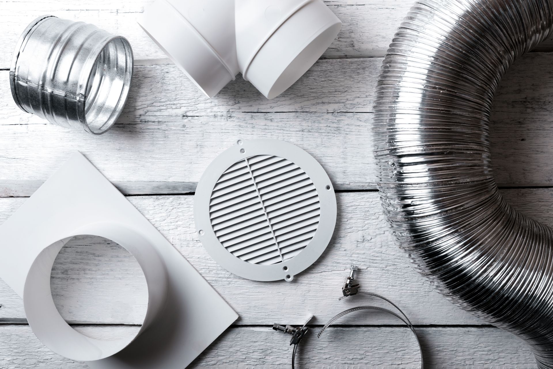 Composants de conduits de CVC : conduits flexibles et rigides, grilles d’aération, connecteurs, colliers de serrage, sur bois blanc.