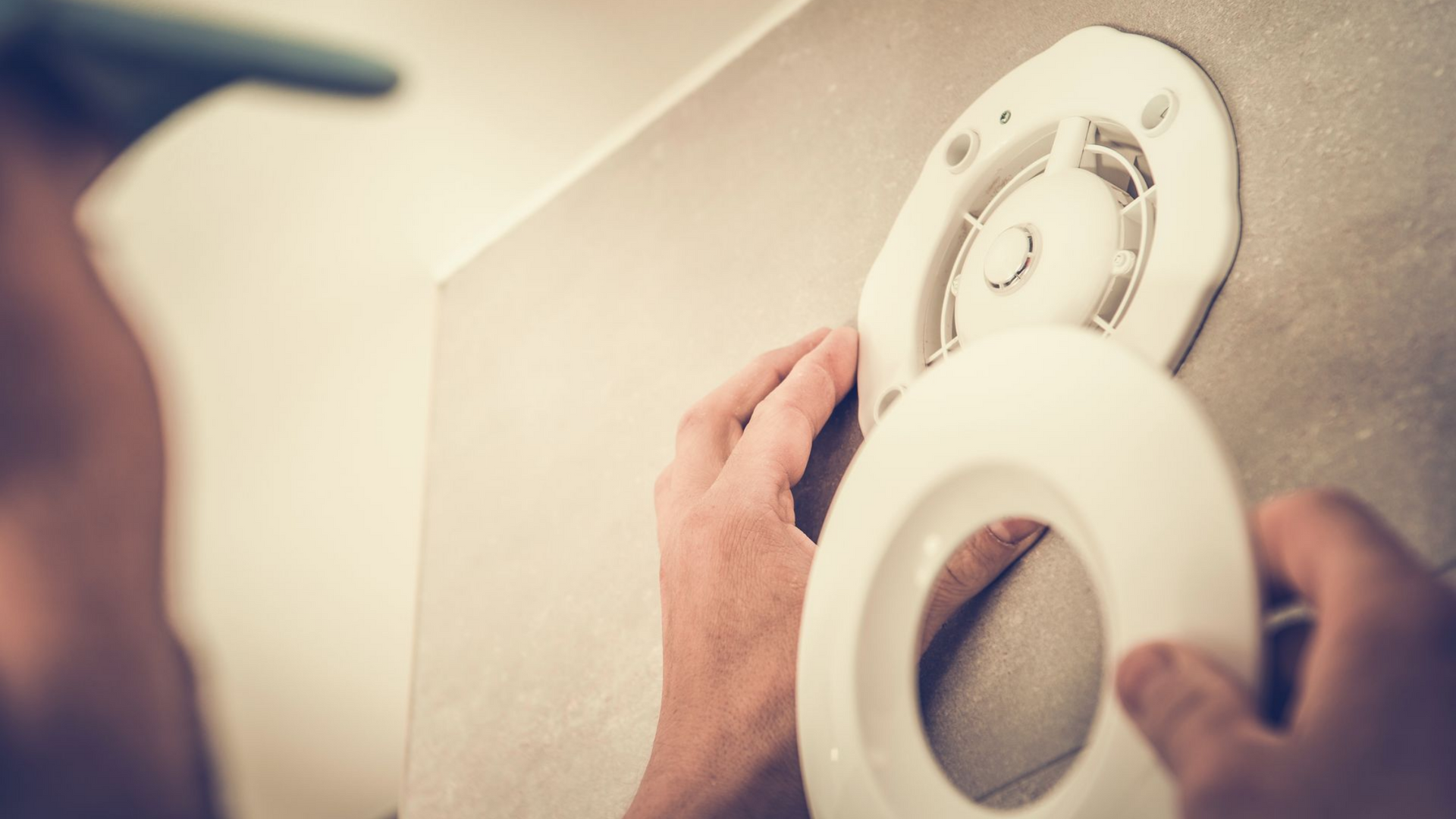 Une personne installe une grille d'aération blanche dans une salle de bain, tenant le couvercle près du mur.