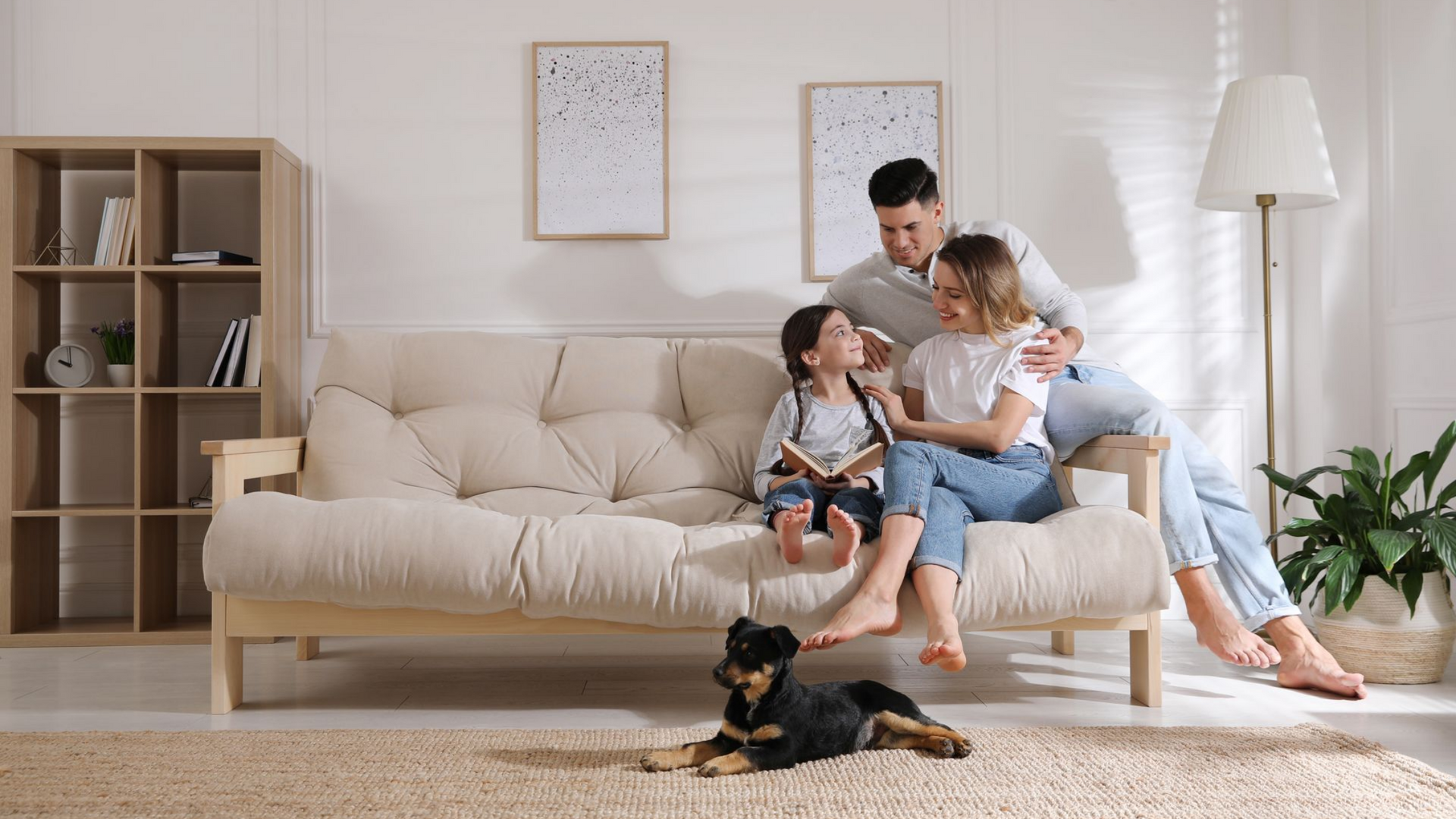 Une famille lit sur un canapé beige, le chien à leurs pieds. Salon chaleureux et lumineux.