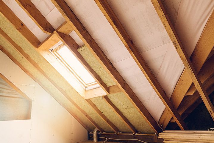 Intérieur du grenier avec poutres en bois, isolation et puits de lumière.