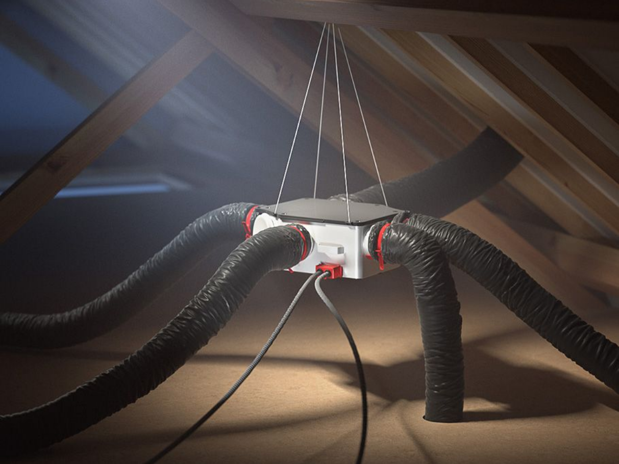 Un système de ventilation dans un grenier. Des tuyaux noirs partent d'une unité centrale blanche, suspendue aux chevrons.