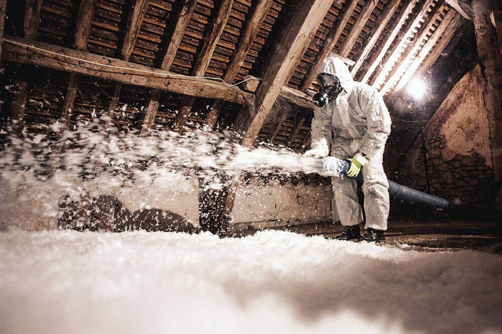 Une personne en combinaison de protection pulvérise de l'isolant dans un grenier.