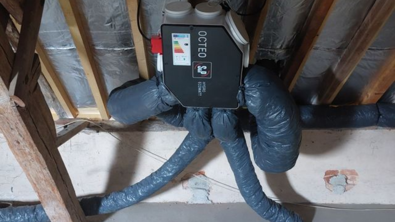 Unité de ventilation installée dans un grenier, avec conduits flexibles isolés raccordés.