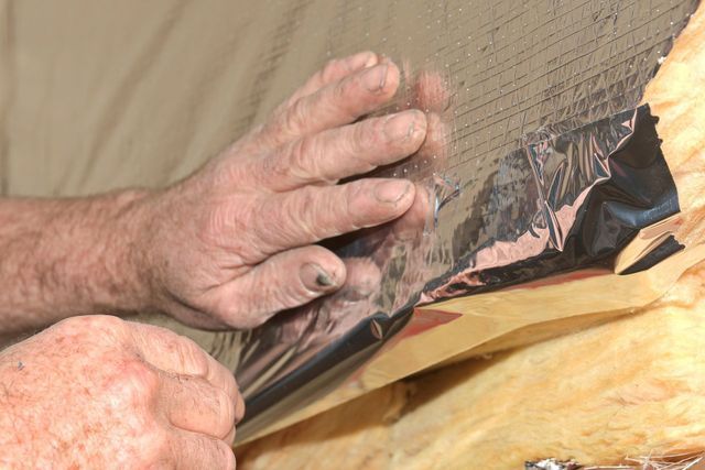 Des mains appliquent un isolant argenté brillant sur une surface en bois, probablement dans un grenier.