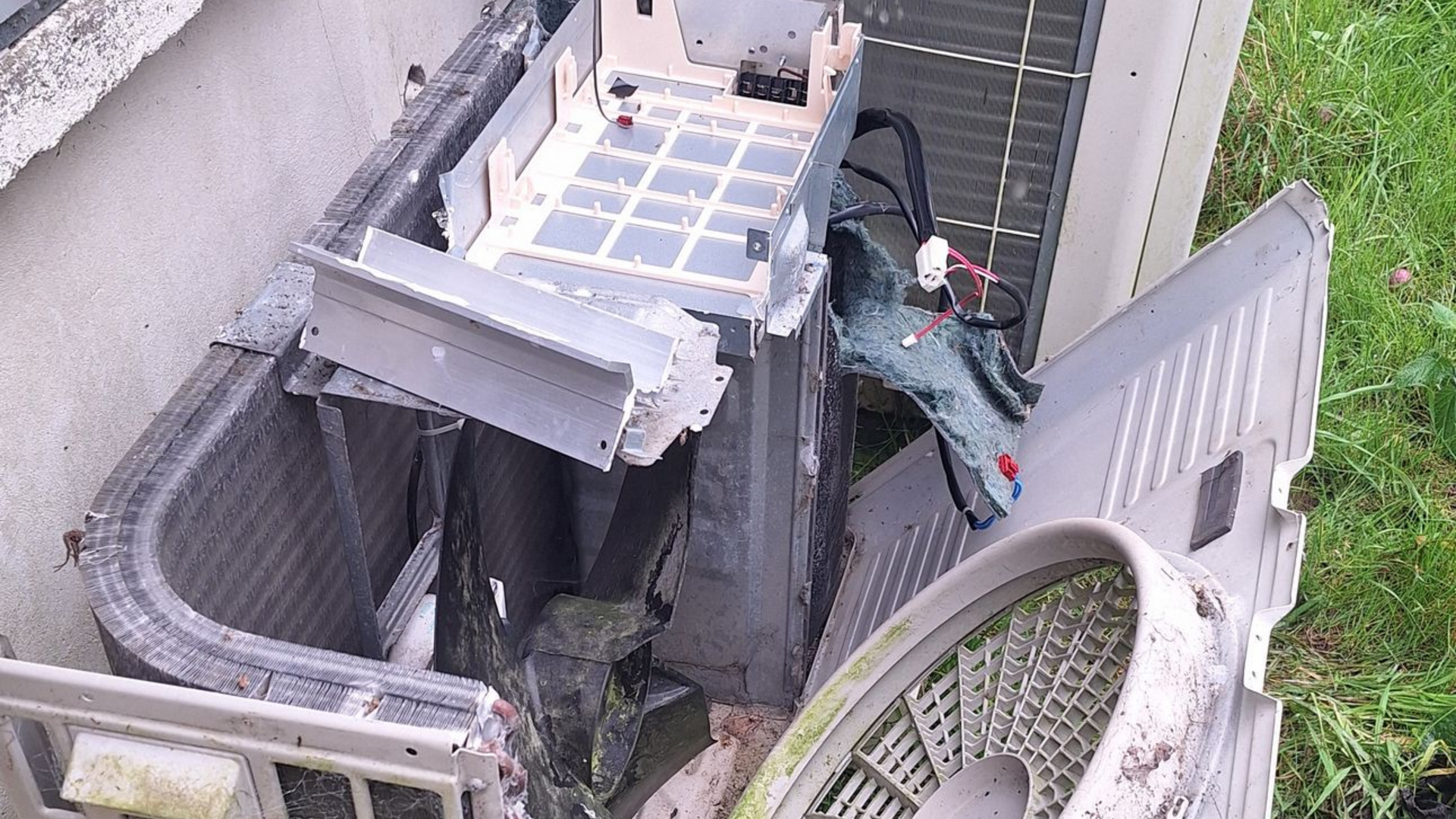 Unité de climatisation endommagée, pièces en plastique et en métal éparpillées au sol.