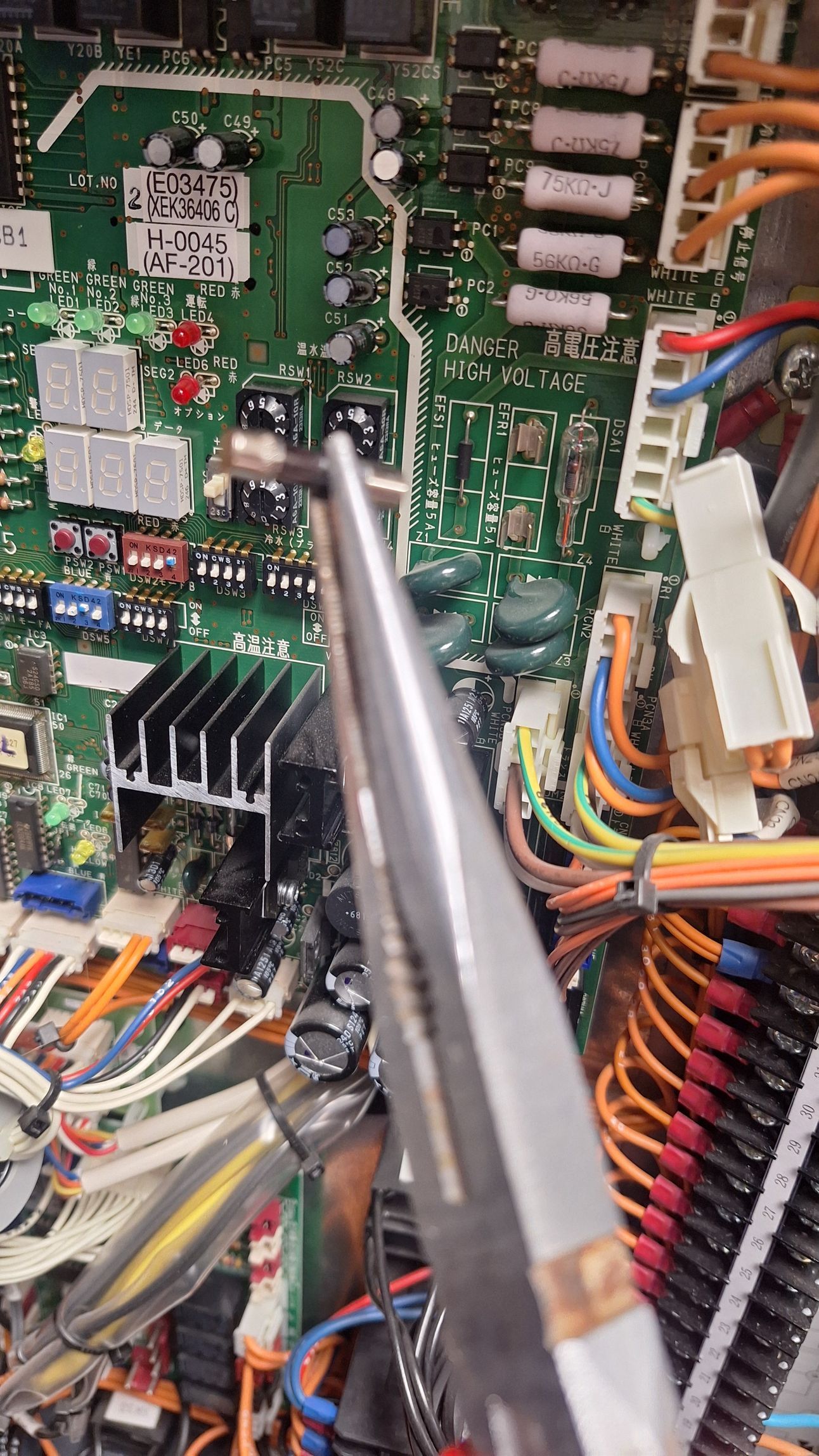 Une personne utilise des pinces pour travailler sur un circuit imprimé avec divers fils et composants.