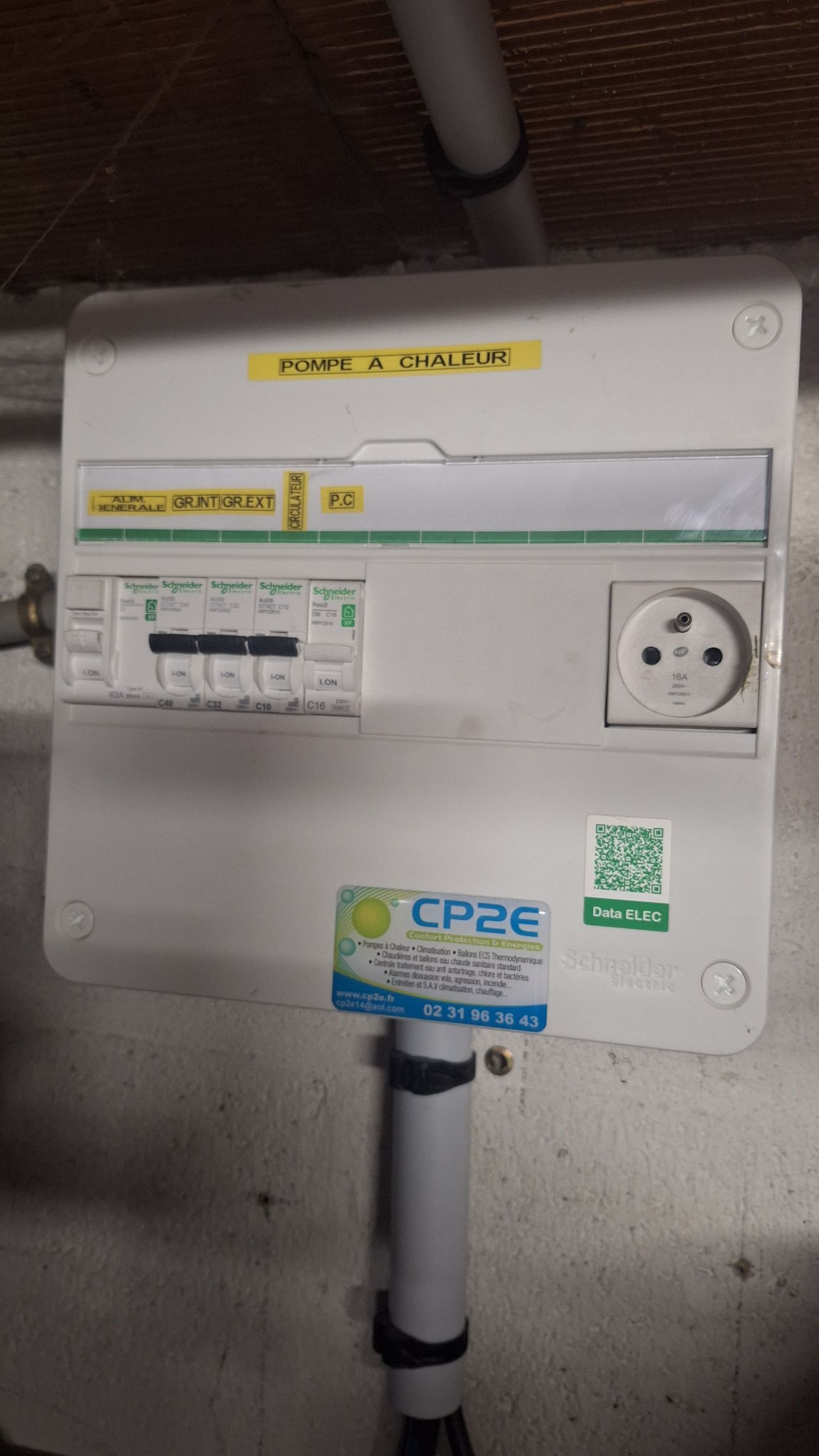 Panneau électrique blanc avec étiquettes et une prise, monté sur un mur en béton.
