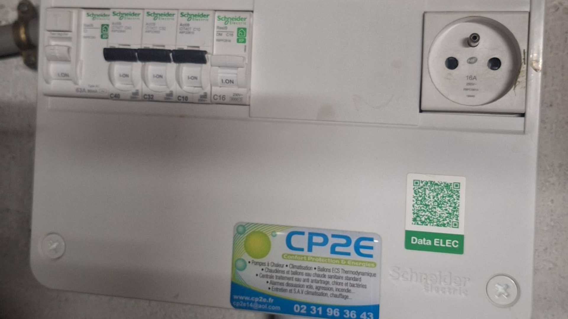Panneau électrique avec disjoncteurs, une prise et des autocollants.
