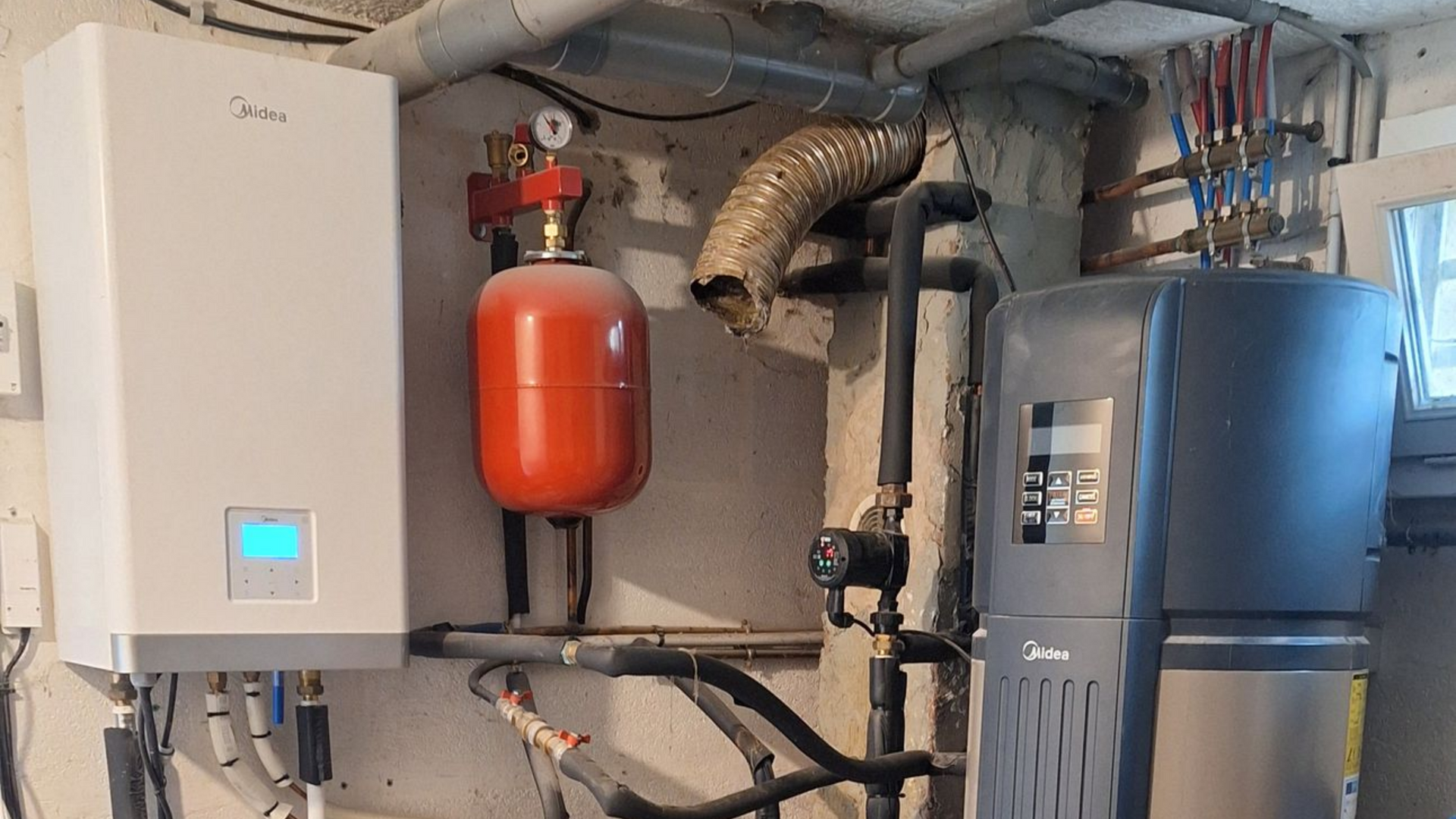 Système de chauffage avec chaudière blanche, réservoir rouge et chauffe-eau gris dans un sous-sol.