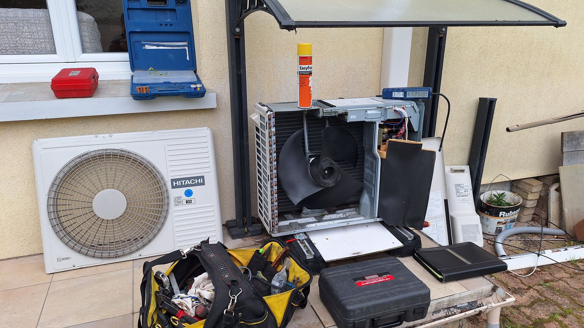 Scène de réparation de CVC avec une unité de climatisation, des outils et des composants disposés à l'extérieur.