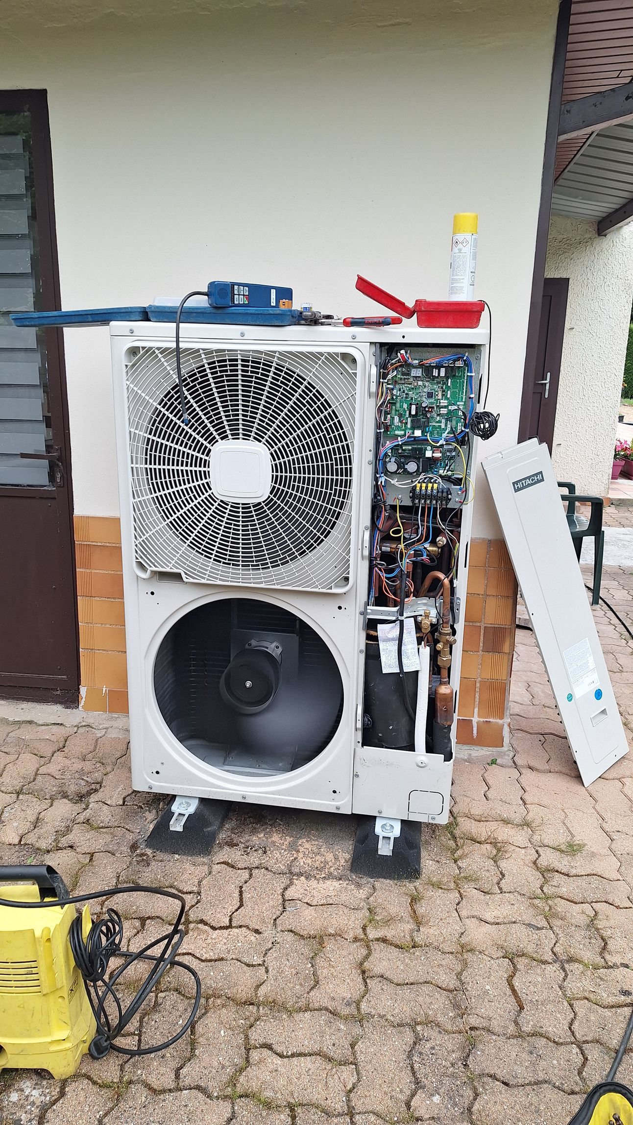 Une thermopompe extérieure dont le panneau est ouvert, laissant apparaître les composants internes.