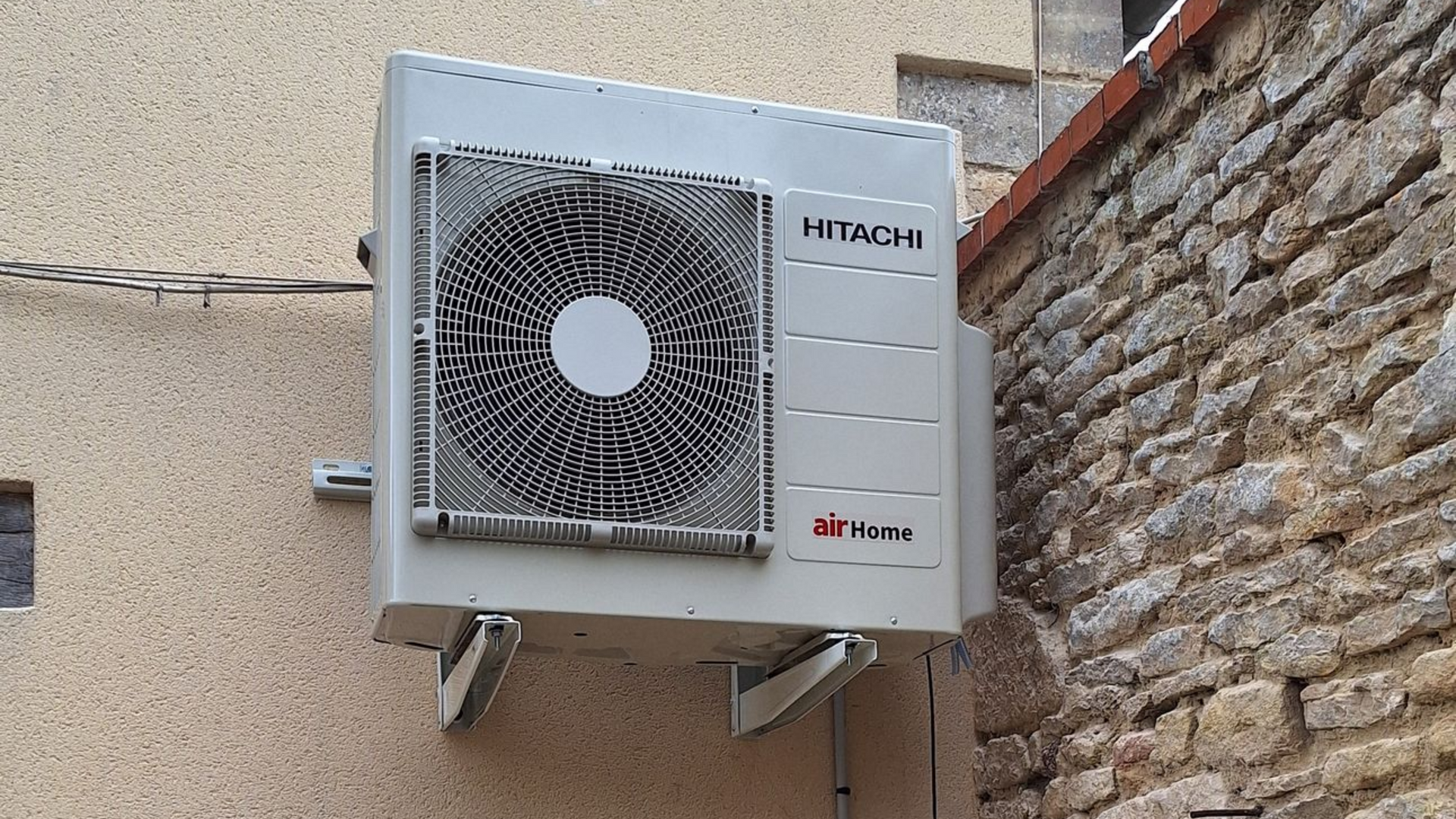 Unité de climatisation Hitachi montée sur des murs extérieurs beiges et pierre.
