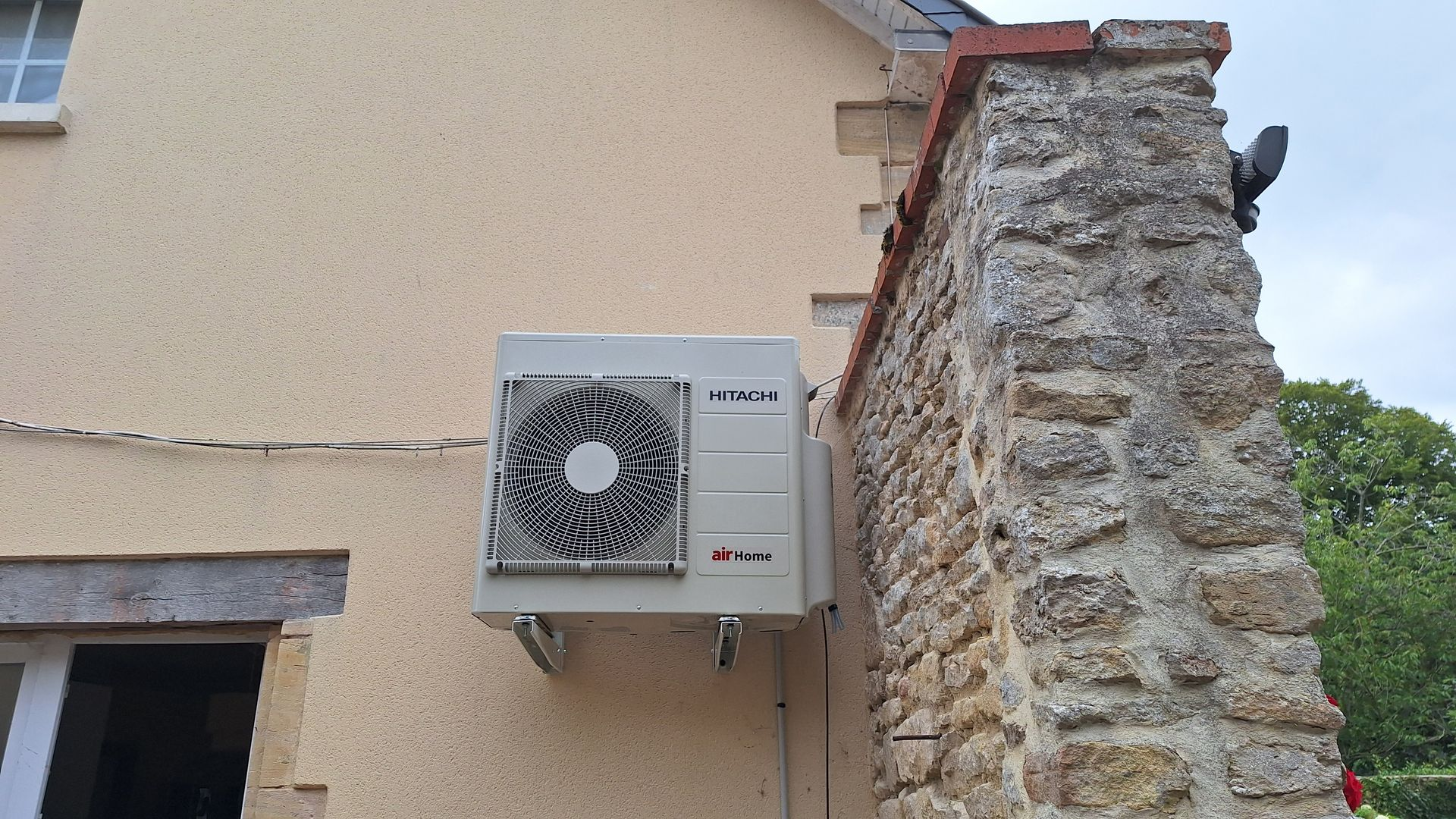 Pompe à chaleur extérieure montée sur un mur beige à côté d'un mur en pierre.