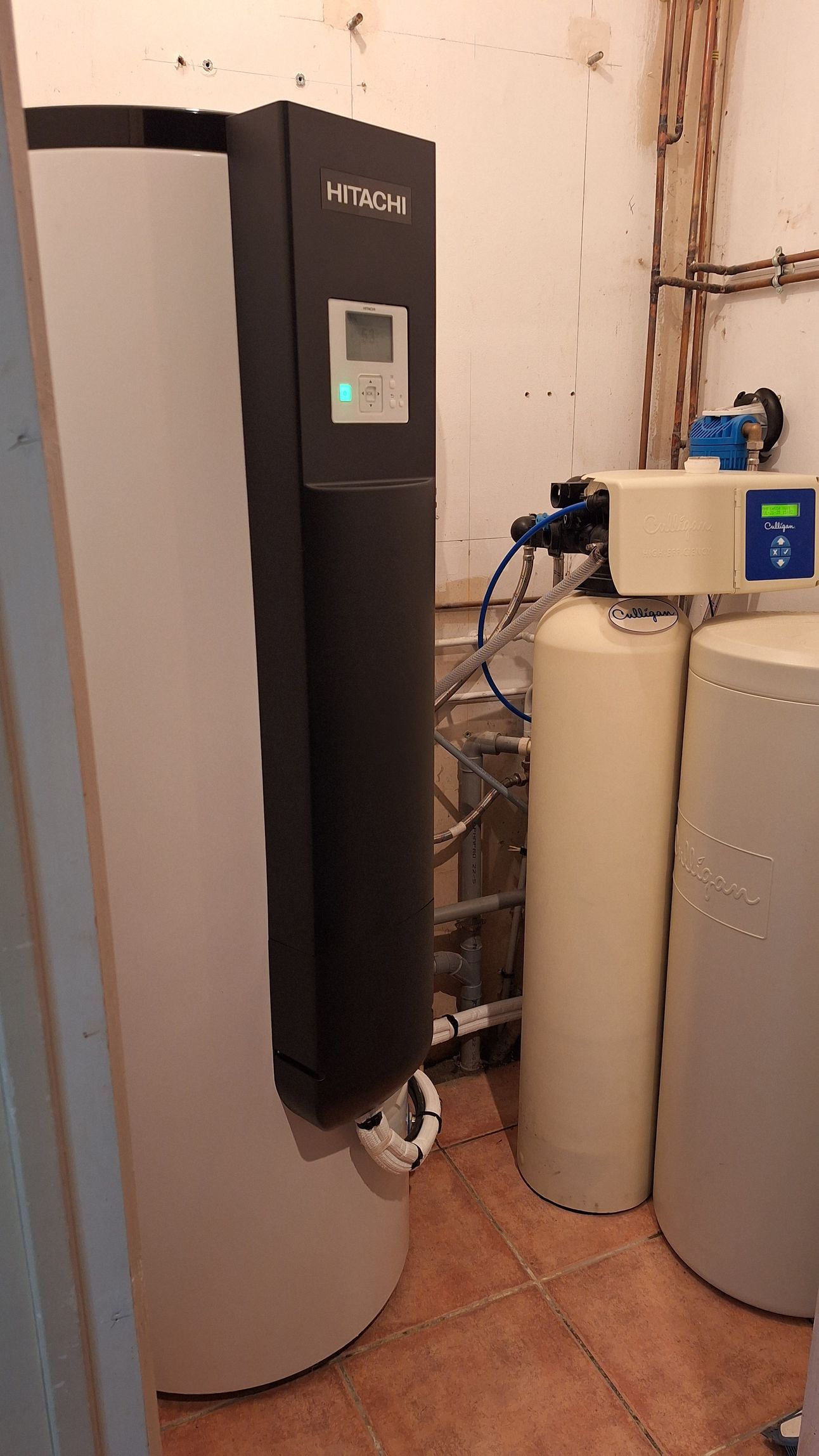 Chauffe-eau et système de filtration dans une buanderie. On distingue des réservoirs blancs et noirs.