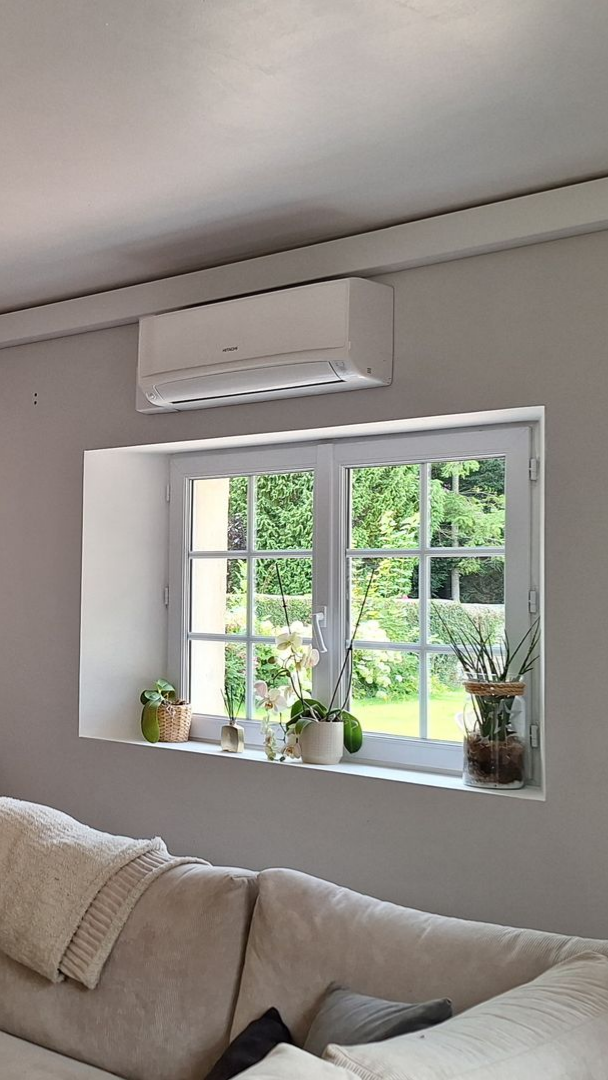 Fenêtre blanche avec plantes en pot et vue sur la verdure ; climatiseur au-dessus.