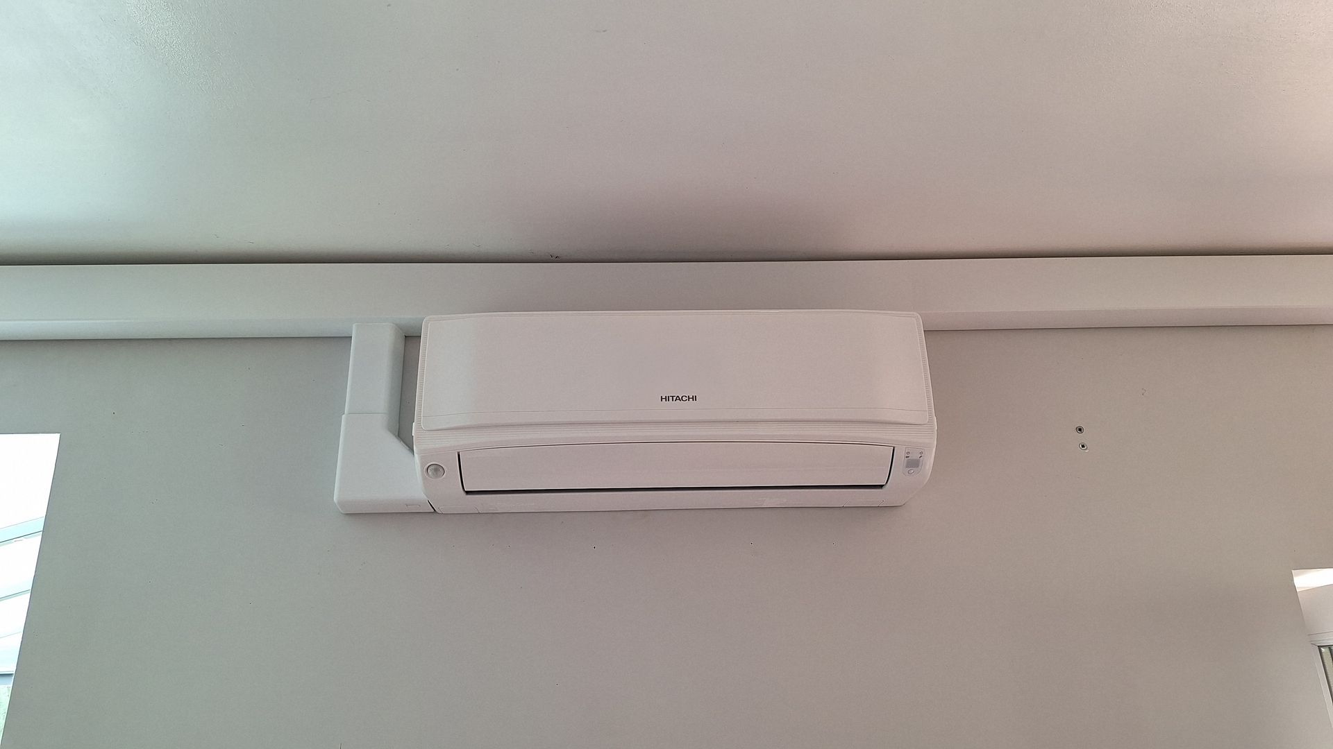 Unité de climatisation blanche montée sur un mur blanc.