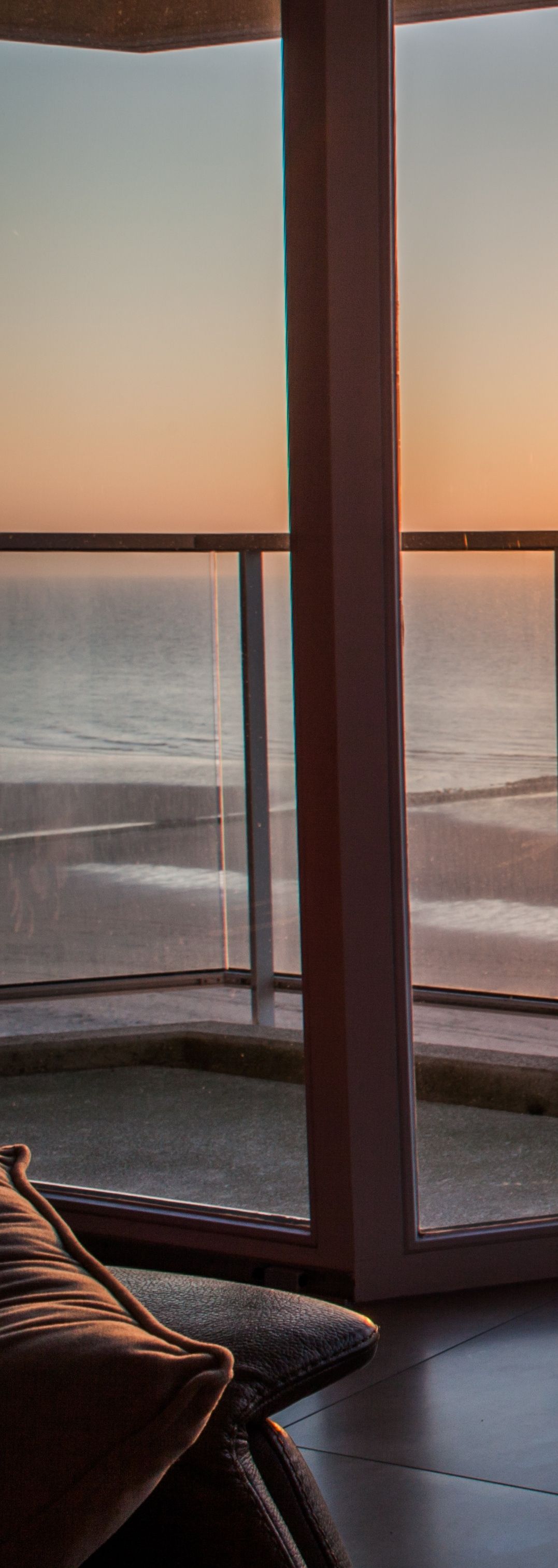 Vue sur l'océan à travers un balcon en verre, avec un oreiller au premier plan.