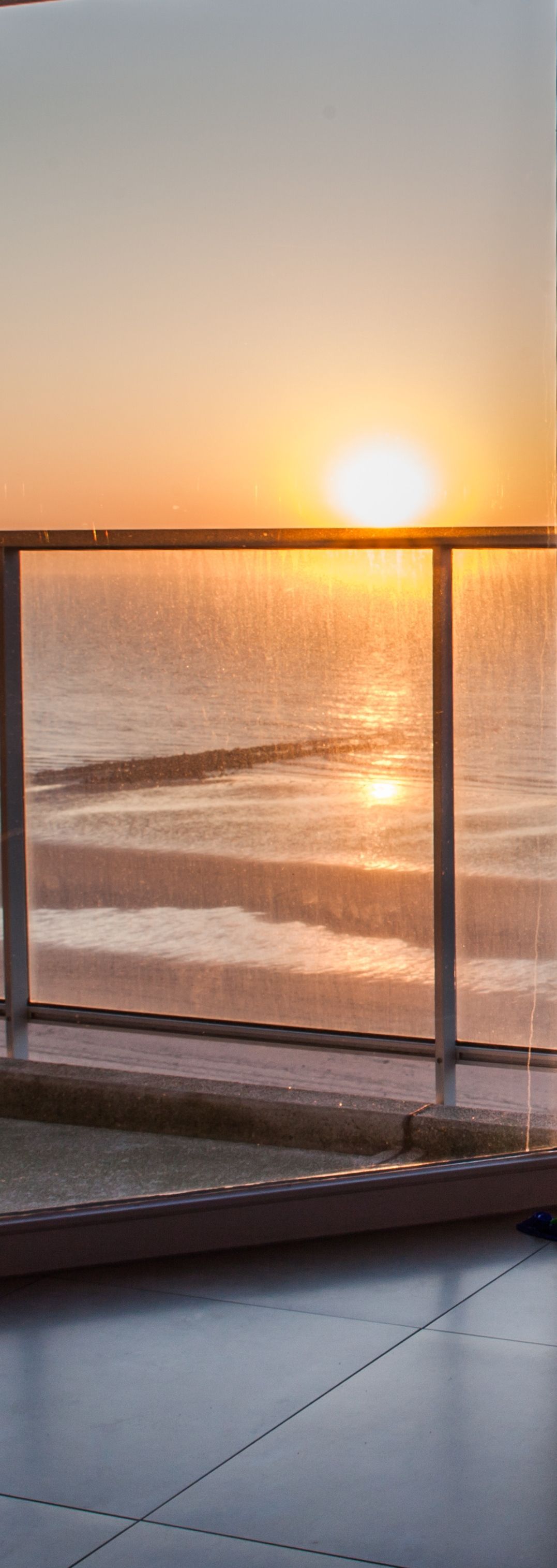 Coucher de soleil sur l'océan vu depuis une terrasse vitrée.