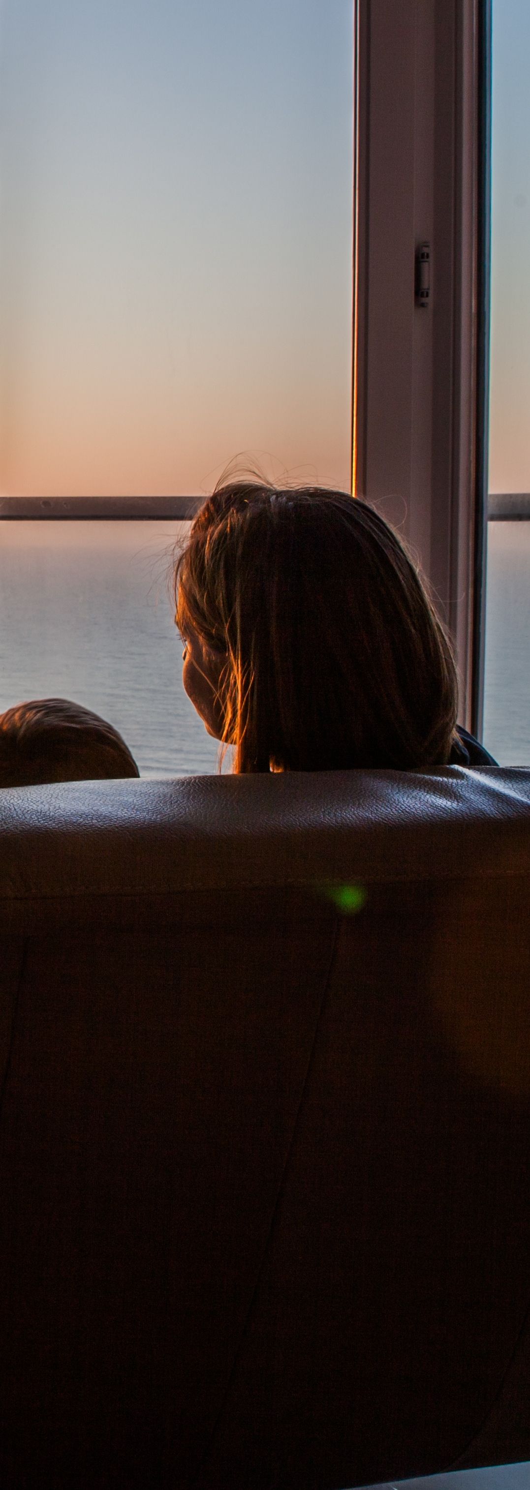 Personne regardant par la fenêtre le coucher du soleil sur l'océan.
