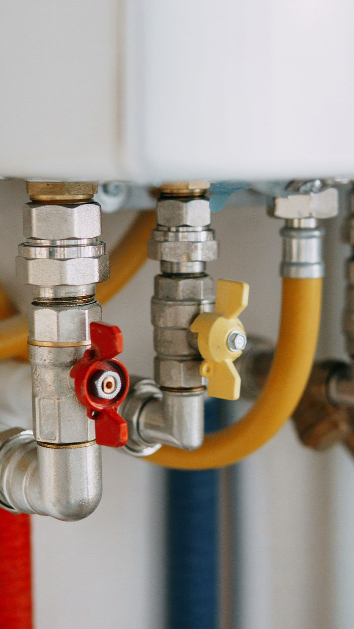 Gros plan d'une chaudière blanche à trois vannes : rouge, jaune et argent. On distingue des tuyaux de différentes couleurs.