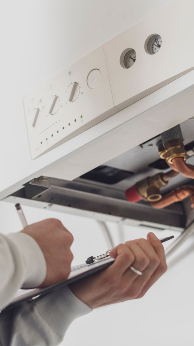 Personne inspectant une chaudière blanche, tenant un presse-papiers et un stylo, documentant l'état de l'appareil.