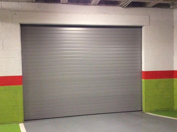 Puerta de garaje gris cerrada en un área de estacionamiento de concreto con paredes pintadas de verde y rojo.
