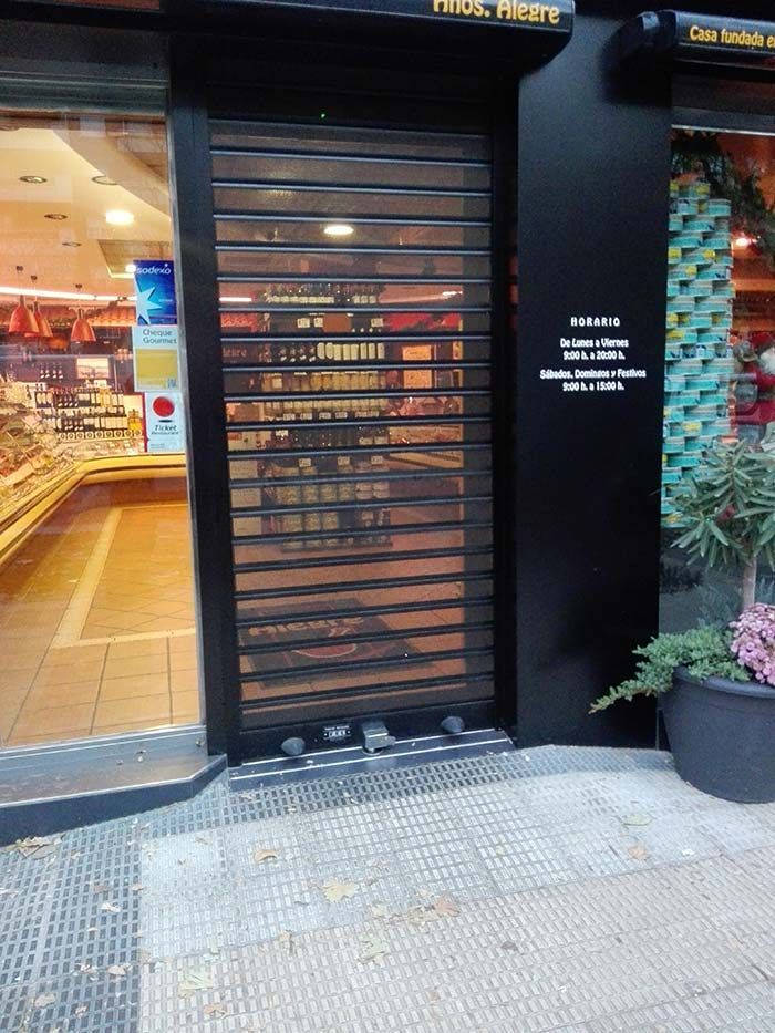 Local comercial cerrado con una puerta de seguridad de metal negro y un interior con iluminación cálida visible desde el interior.