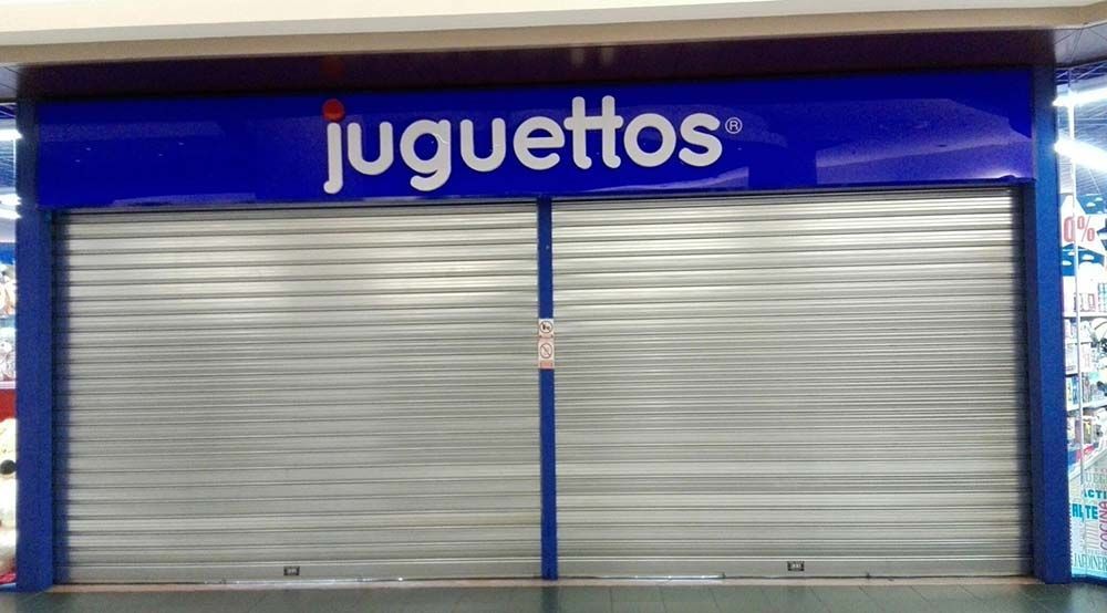 Tienda Juguettos cerrada con fachada azul y contraventanas metálicas plateadas.