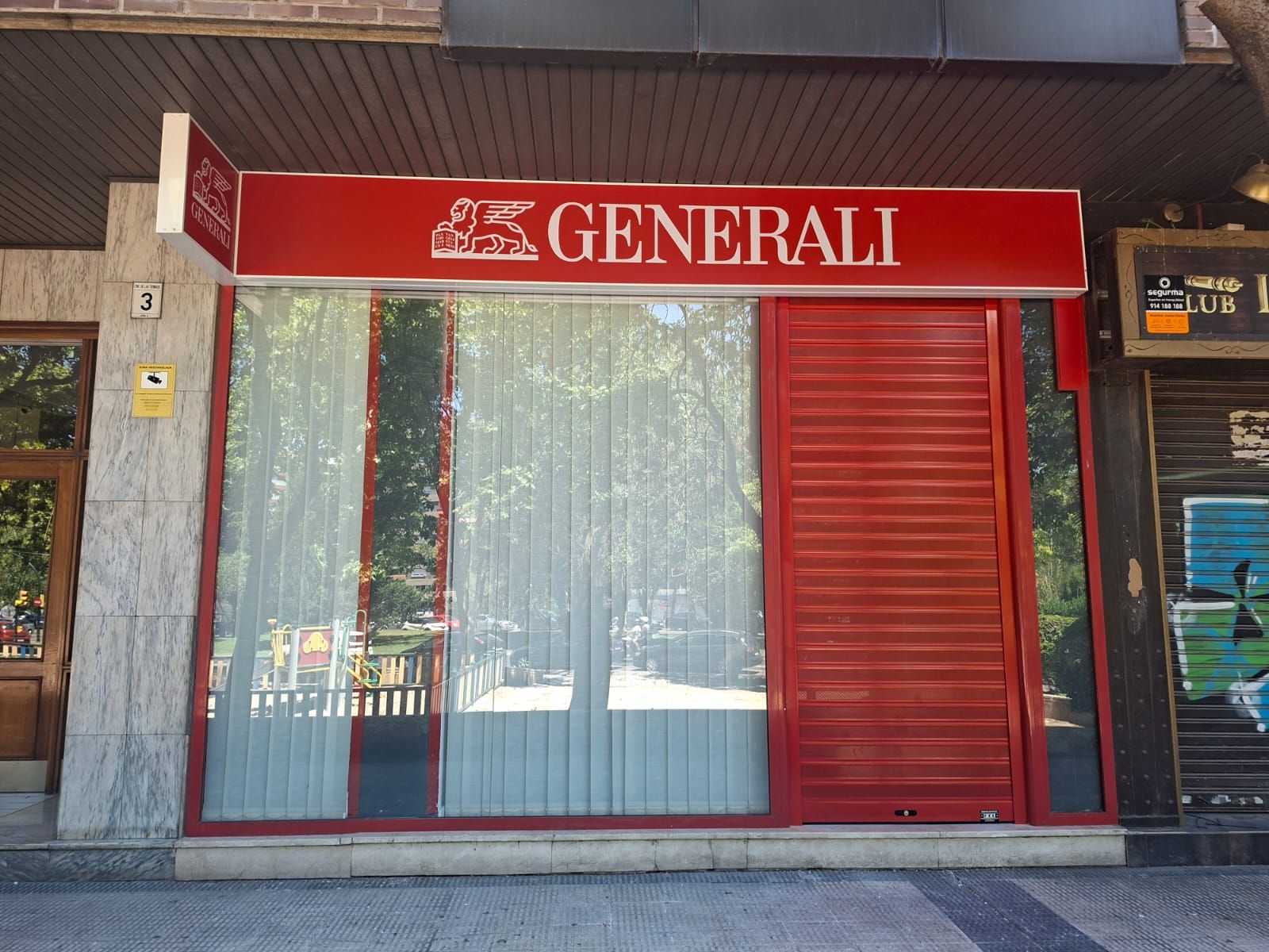 Persiana metálica plateada cerrada con la etiqueta “1” entre dos puertas azules en un área de estacionamiento interior.