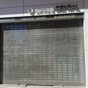 Fachada de una clínica dental cerrada con persiana de seguridad metálica gris y letrero sobre la entrada.