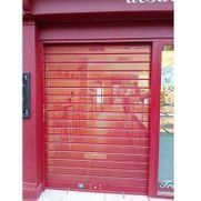 Fachada roja con una persiana metálica enrollable cerrada y paneles de vidrio en los laterales.