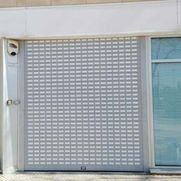 Puerta enrollable metálica gris cerrada junto a una ventana de cristal tintado de azul en la fachada de un edificio.