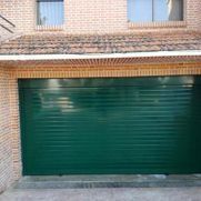 Puerta de garaje metálica verde en la fachada de un edificio de ladrillo.