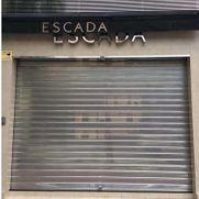 Local comercial cerrado de ESCADA con persiana metálica gris sobre la entrada.