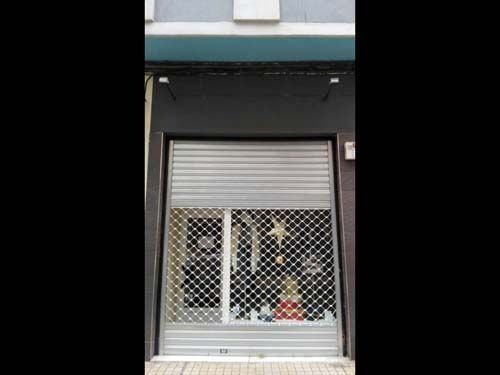 Escaparate con rejas de seguridad metálicas y una persiana gris parcialmente cerrada encima.