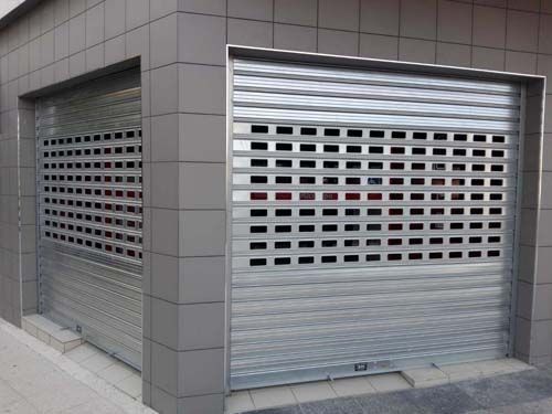 Persianas metálicas cerradas en el escaparate de un edificio de esquina con fachada de azulejos grises.