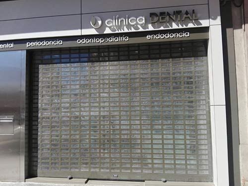 Fachada de clínica dental cerrada con persiana metálica de seguridad y letrero sobre la entrada.