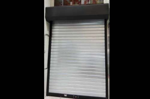 Persiana enrollable plateada cerrada en la fachada de una tienda con un toldo oscuro encima.