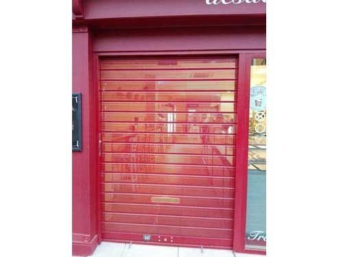 Persiana metálica roja cerrada en la fachada de un edificio rosa.