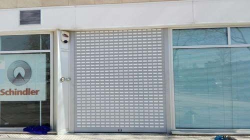 Persianas metálicas cerradas en el escaparate de un edificio de esquina con fachada de azulejos grises.