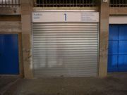 Puerta metálica cerrada en la fachada de un edificio, flanqueada por ventanas azules, con el número 1 encima.
