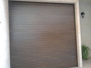Puerta de garaje marrón cerrada en una pared exterior beige.