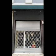Local comercial cerrado con persiana metálica de seguridad y ventana con barrotes, fachada oscura en la parte superior.