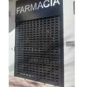 Fachada de farmacia cerrada con reja de seguridad metálica y letrero 