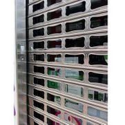 Primer plano de una puerta de seguridad metálica con listones horizontales, que deja ver parcialmente una habitación interior detrás de ella.